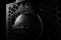 A close-up of a black Beyerdynamic DT 770 Pro over-ear headphone earcup against a dark background with a hexagonal pattern.