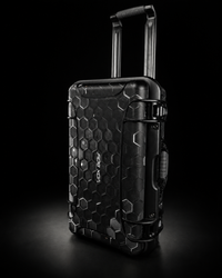 A black hard-shell rolling suitcase with a raised telescoping handle, featuring a textured honeycomb pattern and metallic accents, photographed on a dark studio background.