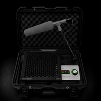 A professional studio sound recording kit in an open black hard carrying case, featuring a shotgun microphone with a gray foam windscreen, a black honeycomb-patterned platform, and a Universal Audio Interface.