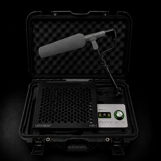 A professional studio sound recording kit in an open black hard carrying case, featuring a shotgun microphone with a gray foam windscreen, a black honeycomb-patterned platform, and a Universal Audio Interface.