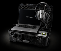 A Vox Boy portable audio device set inside an open black hard case, featuring a silver laptop, over-ear headphones, a silver condenser microphone, and a control module on a black background.