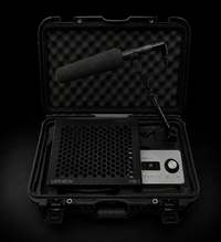 Open black protective carrying case containing a black foam-covered microphone on a stand, a black honeycomb-patterned device labeled VOXBOY, all photographed against a dark black background.