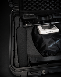 A black foam-covered microphone inside a hard protective carrying case, alongside a white box labeled 'MIC POP FILTER' and a black drawstring bag printed with 'beyerdynamic'.